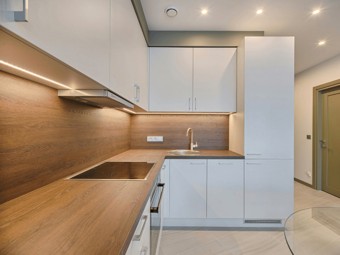 Modern white kitchen with wood countertops and backsplash, built-in stove and oven, and tall pantry cabinet under warm lighting.